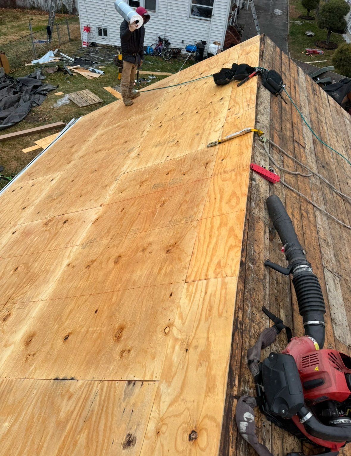 Worker installing plywood roof sheathing on residential house during construction, with power tools visible