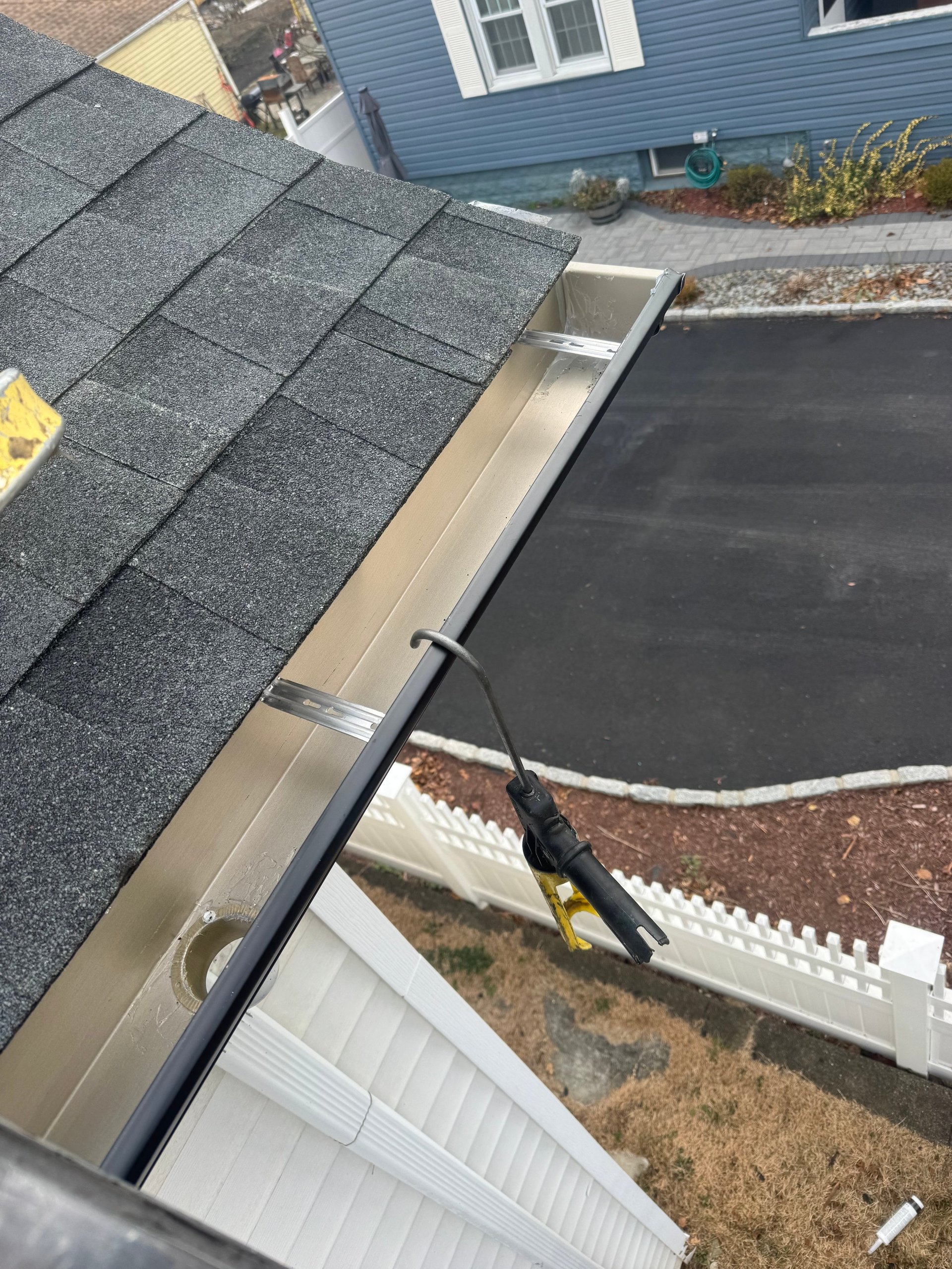 Aerial view of roof installation showing gray shingle roofing, metal gutter, and flat roof membrane on residential home