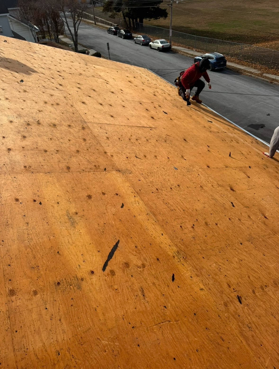 Person in red jacket descending a steep sandy slope toward a residential street with parked cars below