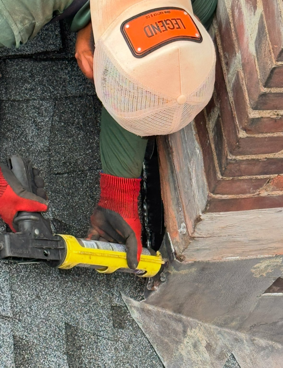 Worker in white hard hat and red socks using a yellow pry bar on asphalt shingles during roof repair