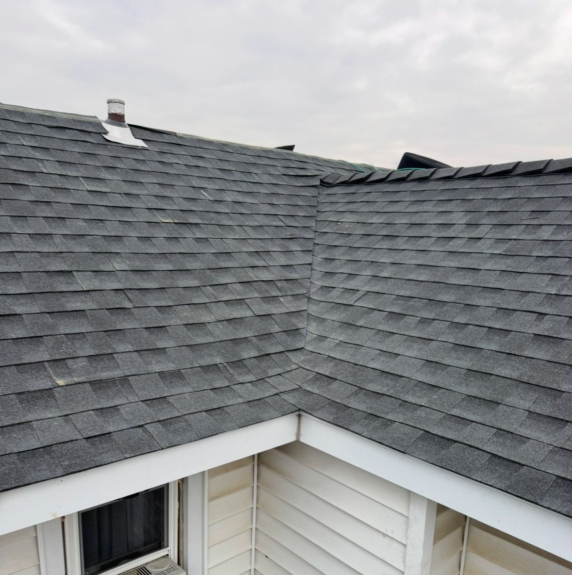 Gray asphalt shingle roof with white trim and valleys meeting at a corner angle under cloudy sky