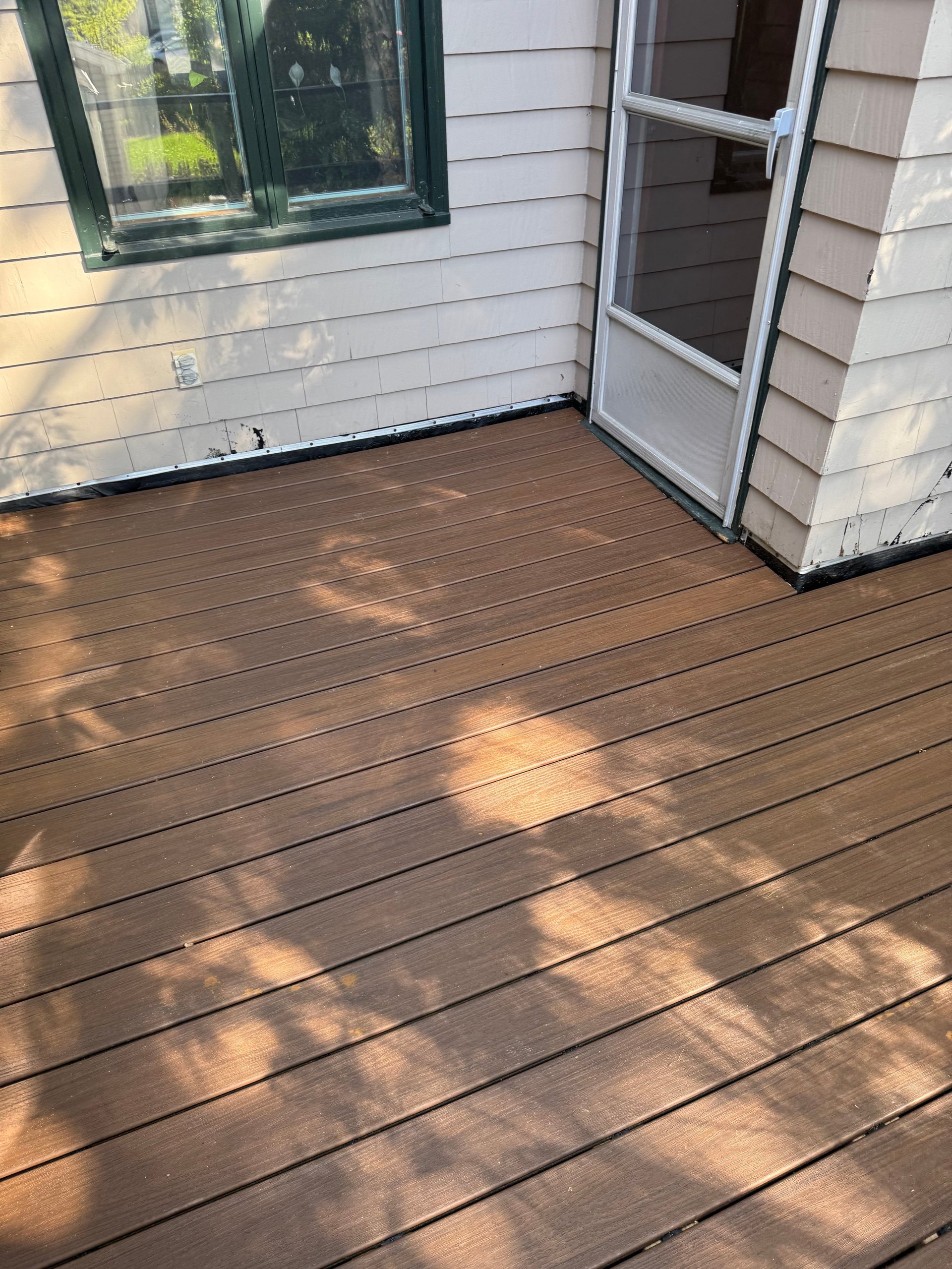 Wooden deck with dappled sunlight attached to a white house with windows and glass door